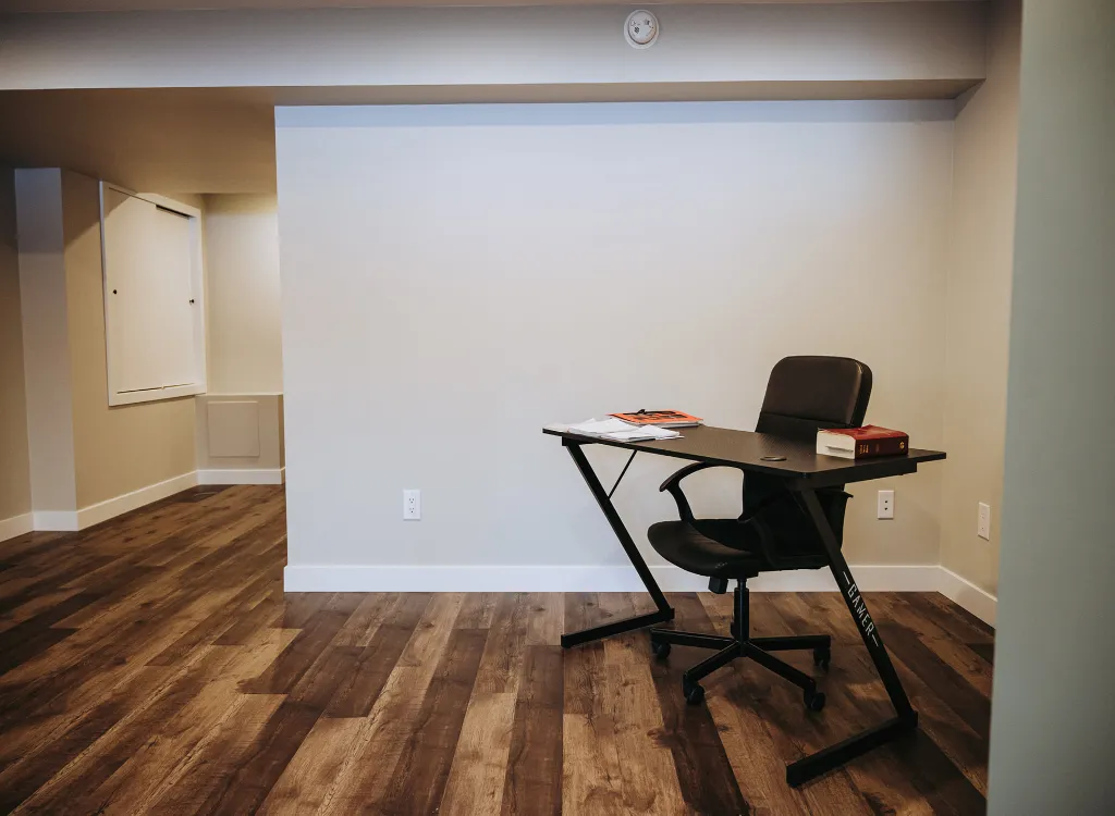 A small desk and office chair sits in a finished basement.